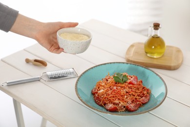 Photo of Food stylist holding grated cheese for spaghetti at white wooden table in studio, closeup