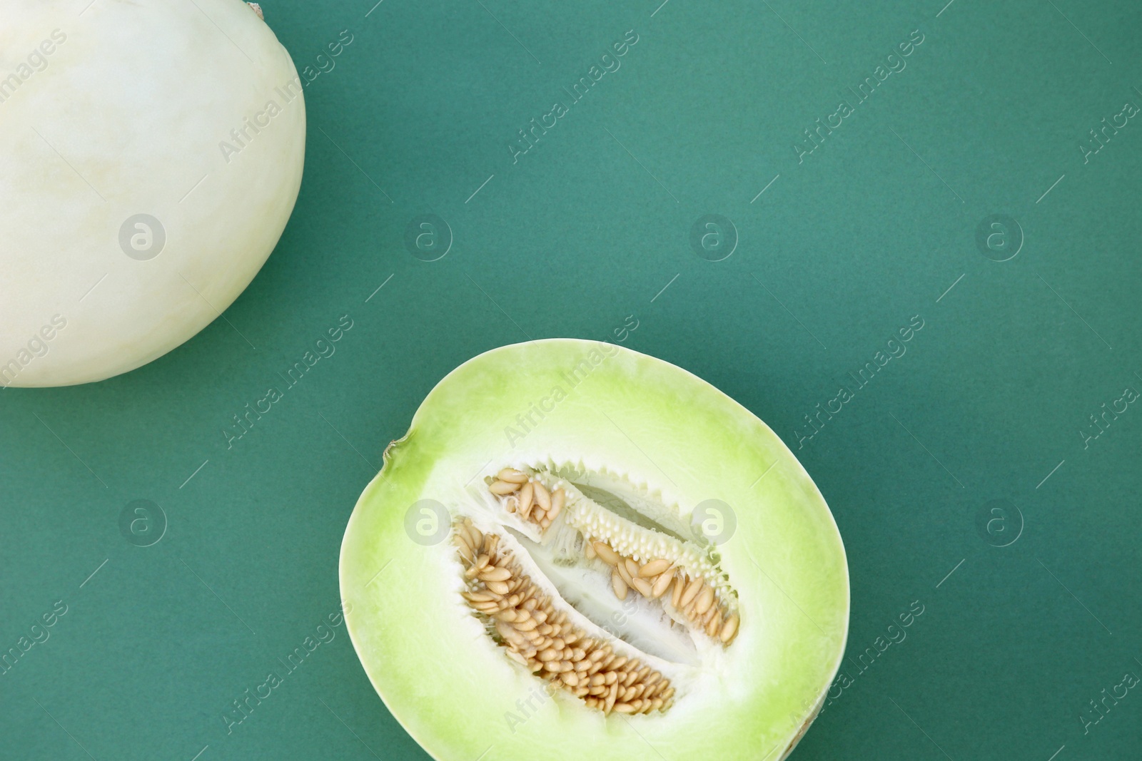 Photo of Whole and cut fresh ripe honeydew melons on teal background, flat lay. Space for text