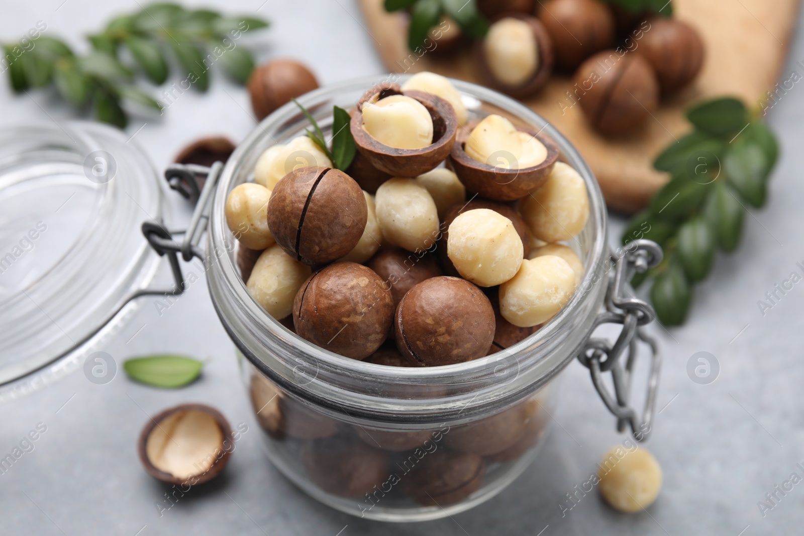 Photo of Tasty Macadamia nuts in jar on light grey table, closeup