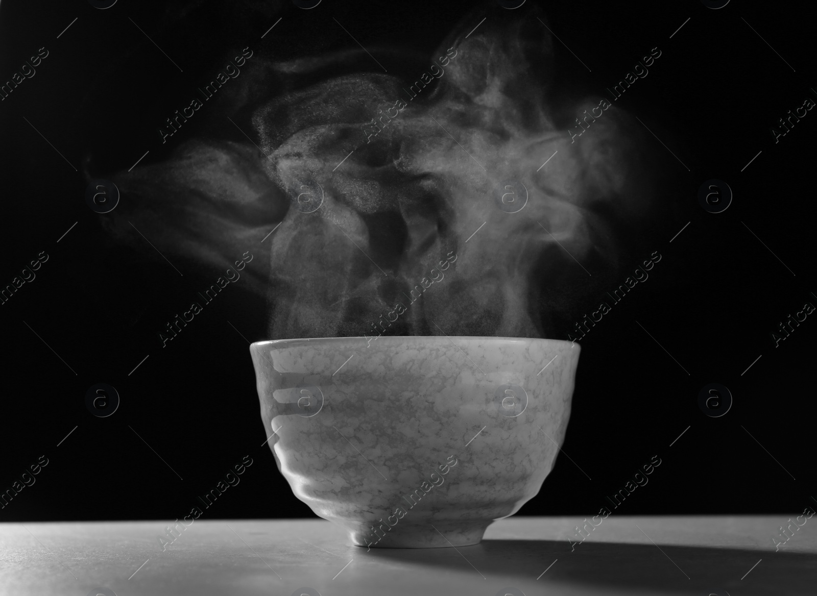 Photo of Bowl with steam on table against black background