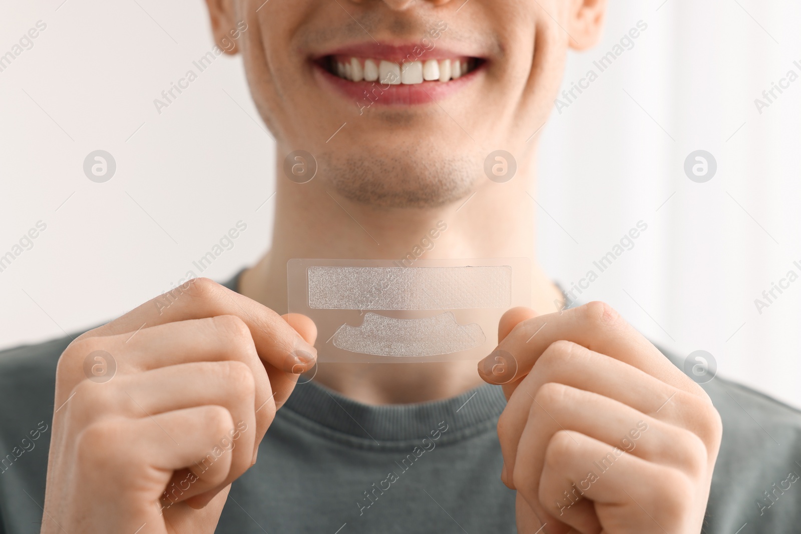Photo of Young man with whitening strips on light background, closeup