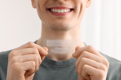 Young man with whitening strips on light background, closeup