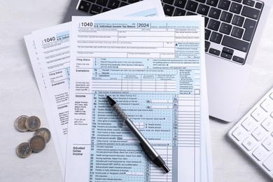 Photo of Tax forms, coins, pen, laptop and calculator on light grey table, flat lay