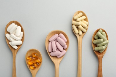 Different vitamin pills in spoons on light grey background, flat lay. Health supplement