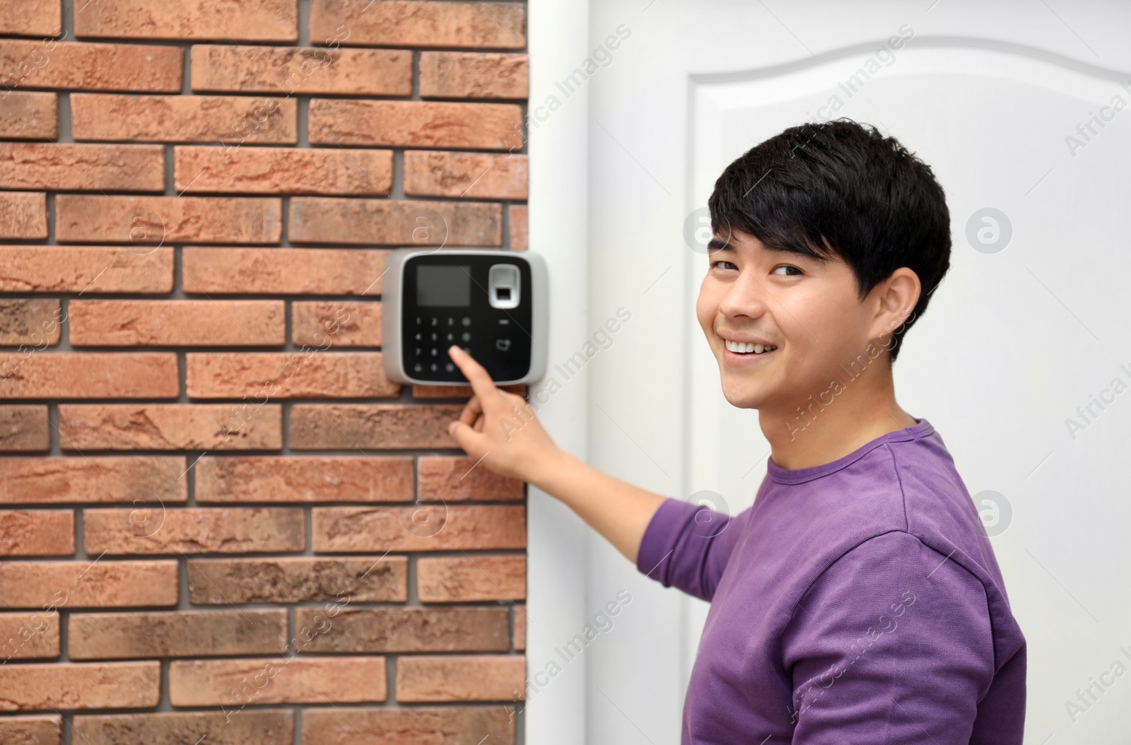 Photo of Young man entering code on alarm system keypad indoors