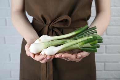 Photo of Woman holding green spring onions near white brick wall, closeup