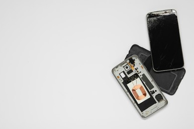 Photo of Damaged smartphone on white background, flat lay with space for text. Device repairing