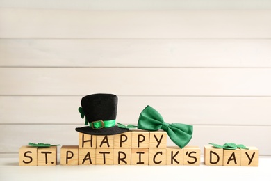 Photo of Leprechaun hat, green bow tie and wooden cubes with words Happy St Patrick's Day on white table, space for text