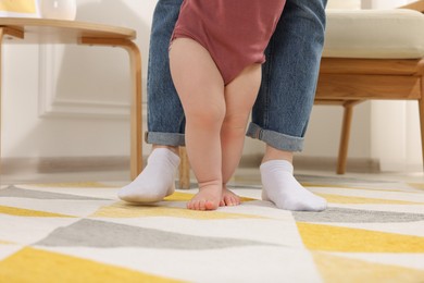 Photo of Mother supporting her baby son while he learning to walk on carpet at home, closeup