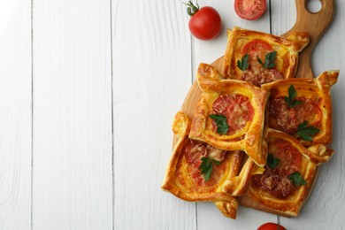 Fresh delicious puff pastry with cheese, tomatoes and parsley on white wooden table, flat lay. Space for text