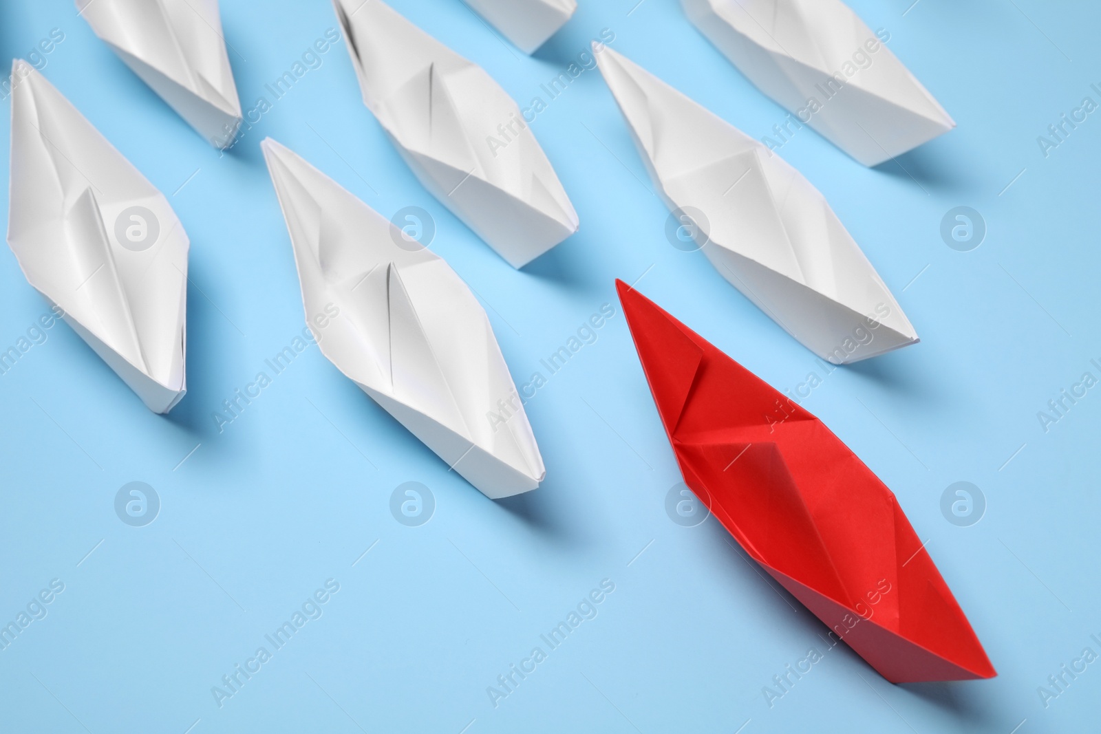 Photo of Paper boats following red one on light blue background. Leadership concept