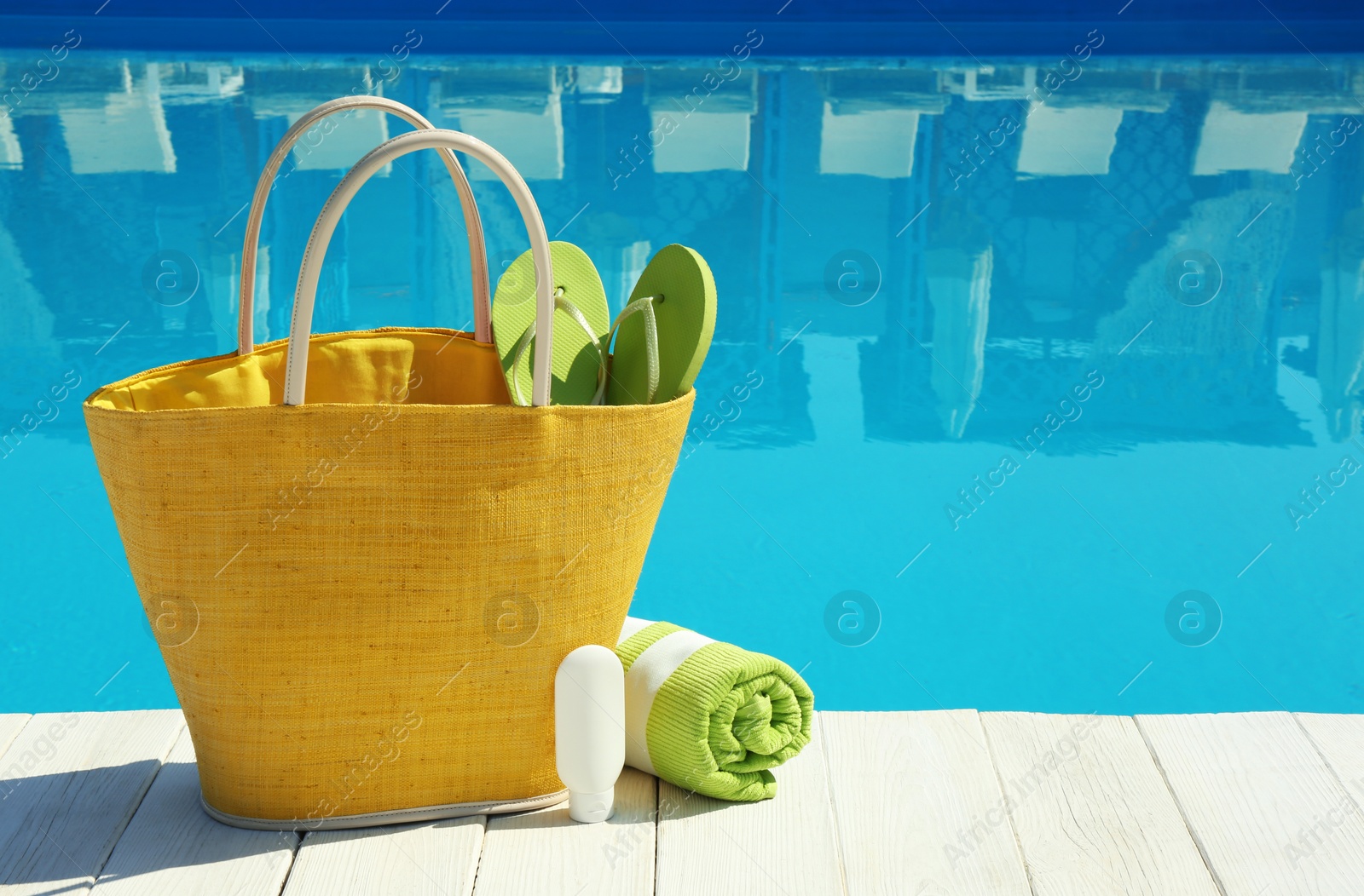 Photo of Beach accessories on wooden deck near swimming pool. Space for text