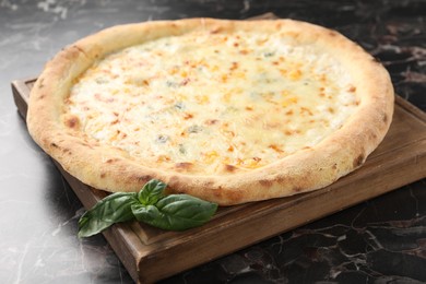 Photo of Delicious cheese pizza and basil on black marble table, closeup