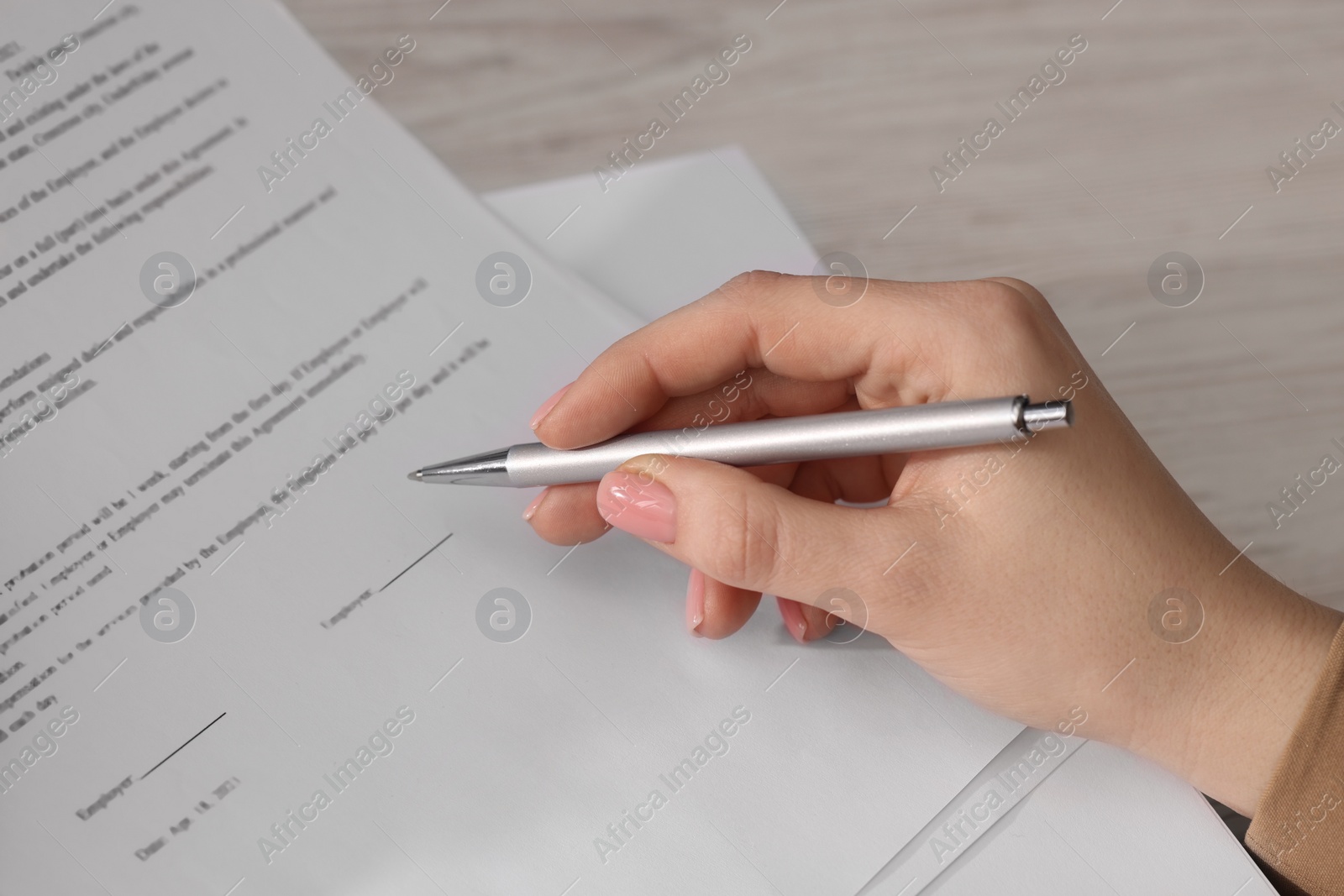 Photo of Woman signing document at wooden table, closeup