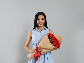 Happy woman with red tulip bouquet on light grey background. 8th of March celebration