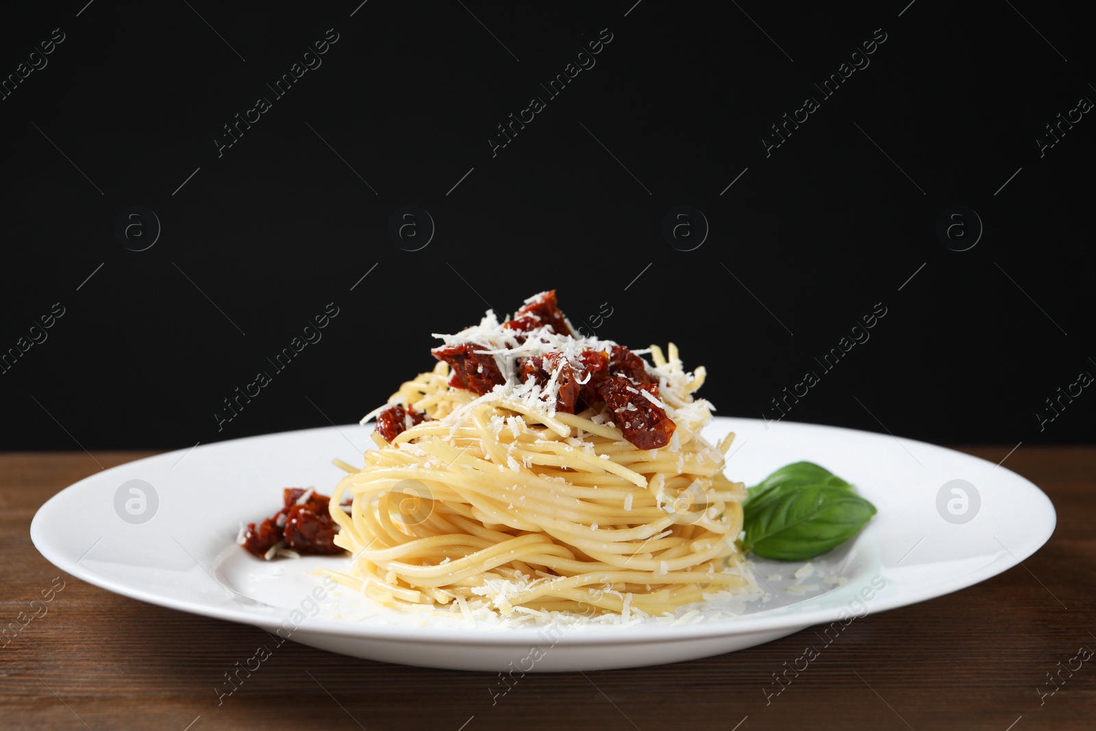 Photo of Tasty spaghetti with sun-dried tomatoes and parmesan cheese on wooden table, closeup. Exquisite presentation of pasta dish