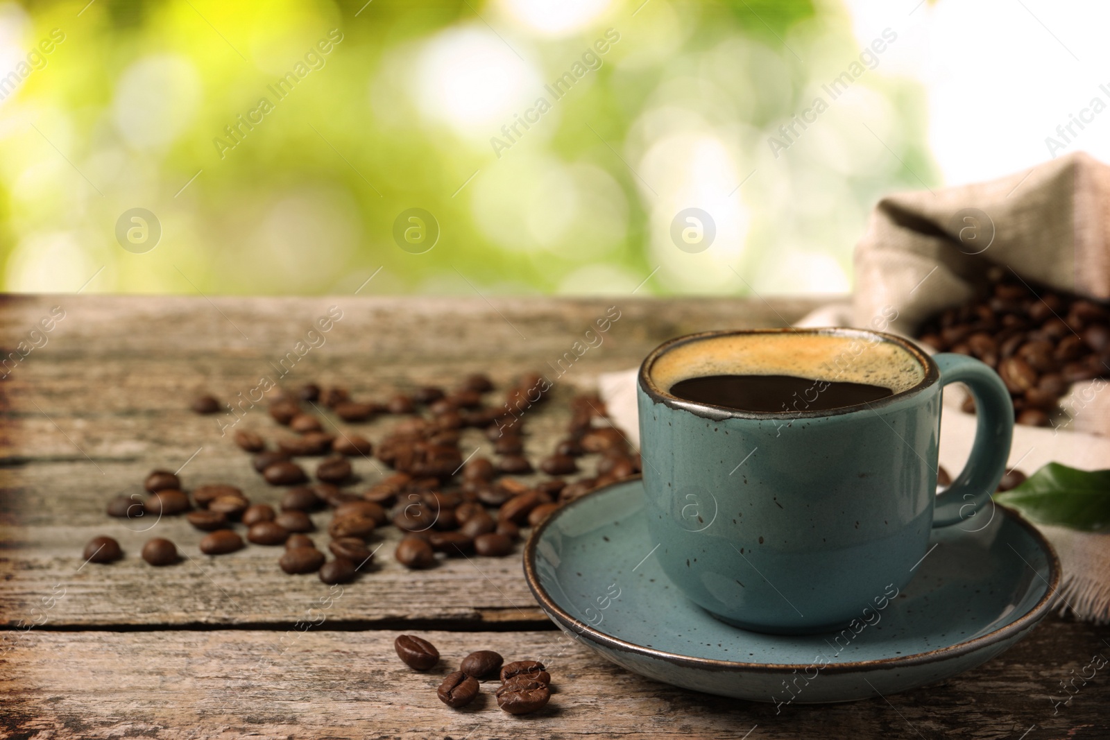 Image of Cup of aromatic hot coffee and beans on wooden table outdoors. Space for text