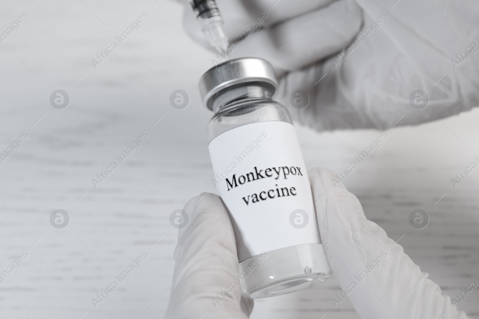 Photo of Nurse filling syringe with monkeypox vaccine from vial at white wooden table, closeup