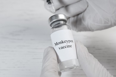 Nurse filling syringe with monkeypox vaccine from vial at white wooden table, closeup