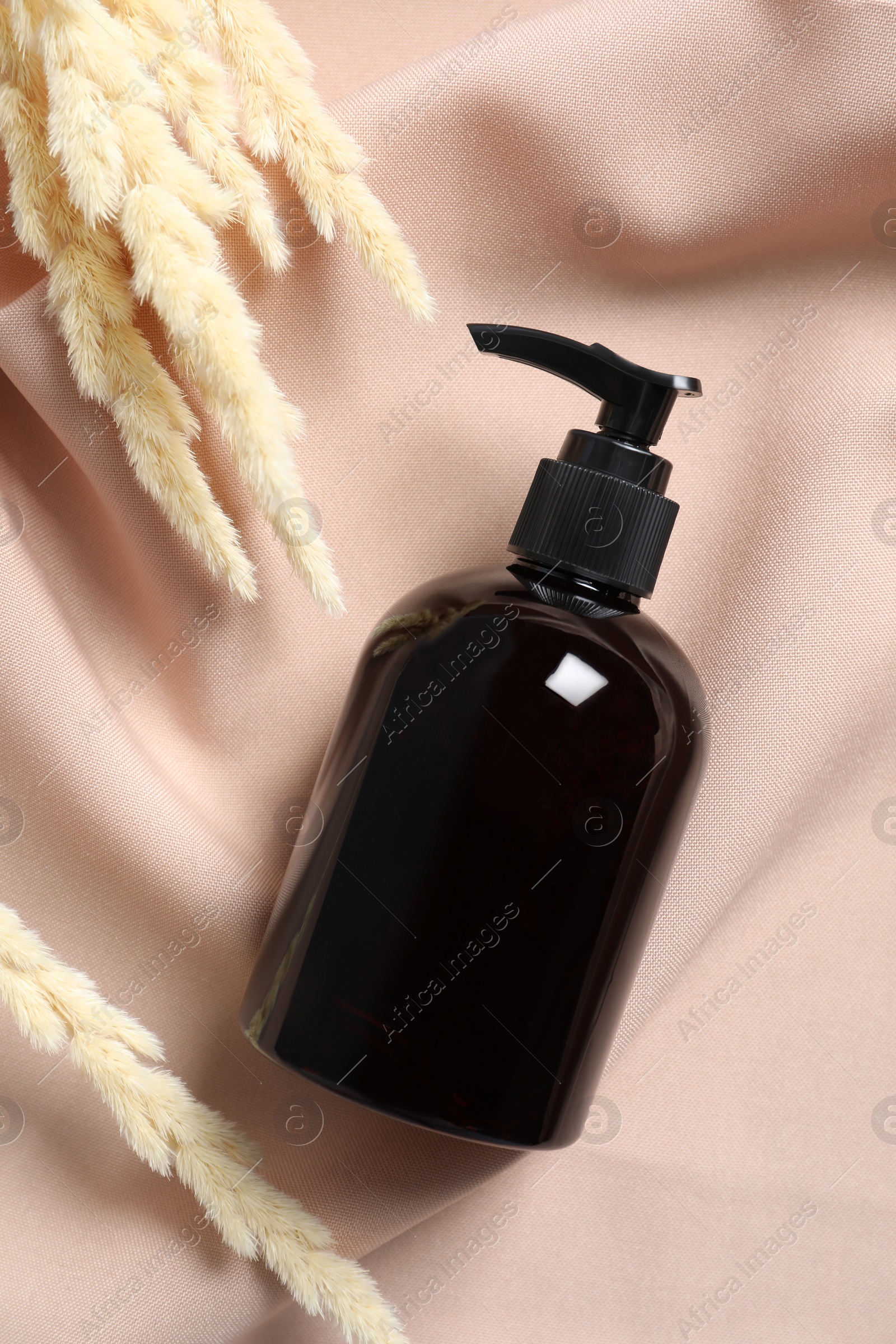 Photo of Bottle of cosmetic product and dry spikes on pink fabric, flat lay