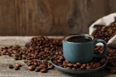 Photo of Cup of aromatic coffee and beans on wooden table. Space for text