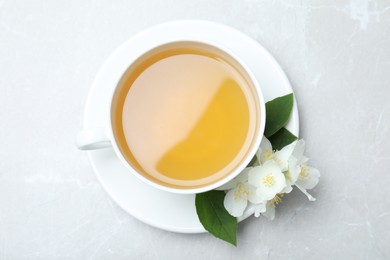 Photo of Cup of tea and fresh jasmine flowers on light grey marble table, top view