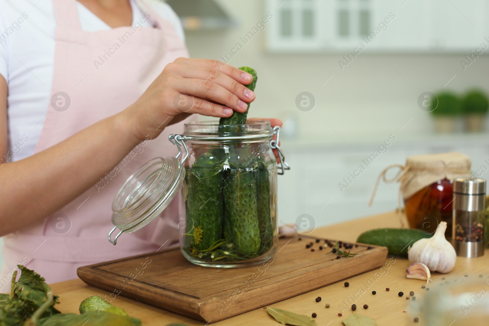 Photo of Woman putting cucumber into pickling jar at table in kitchen, closeup