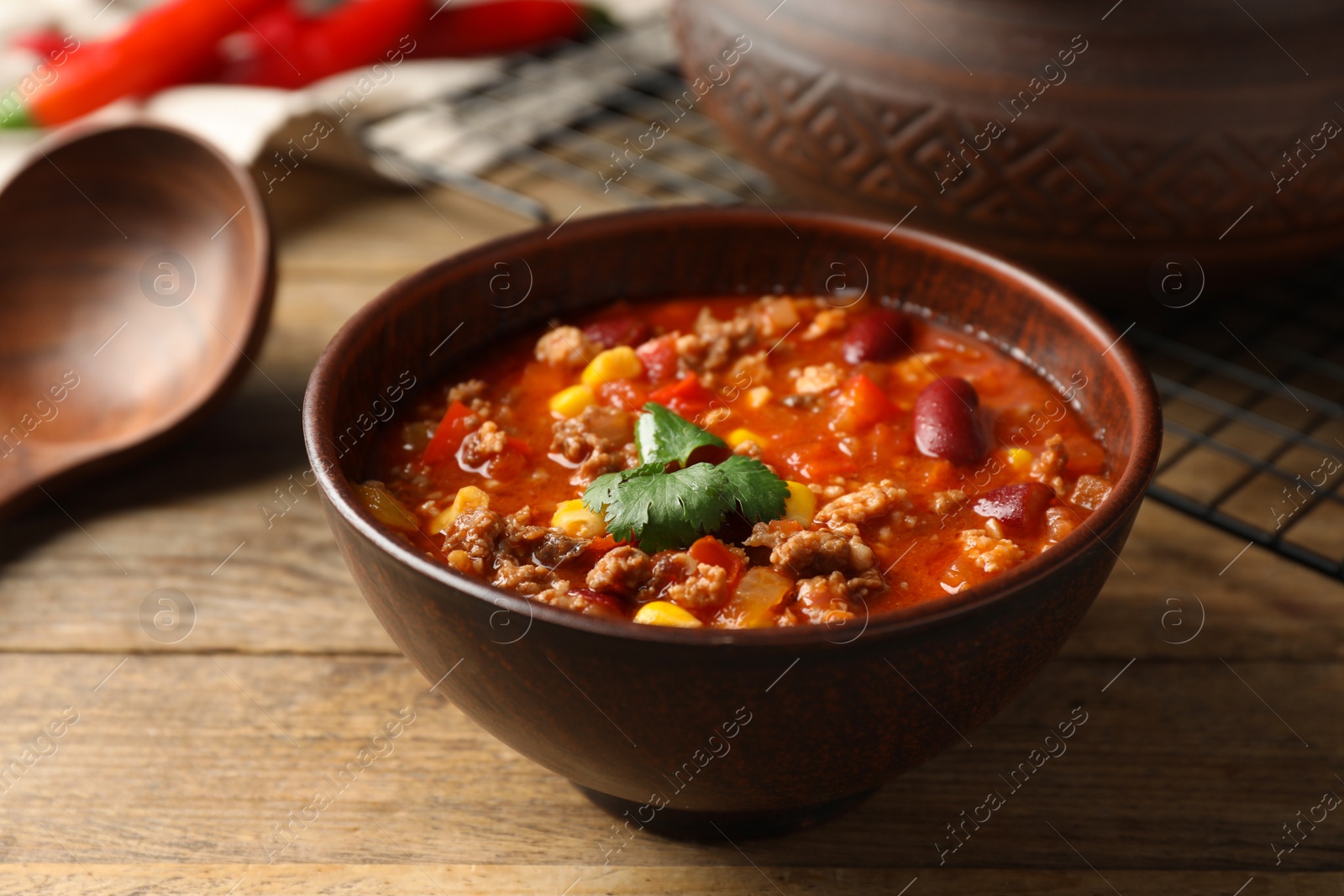 Photo of Bowl with tasty chili con carne on wooden table, closeup