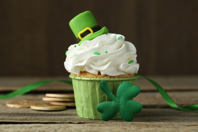 Photo of St. Patrick's day party. Tasty cupcake with green leprechaun hat topper on wooden table, closeup