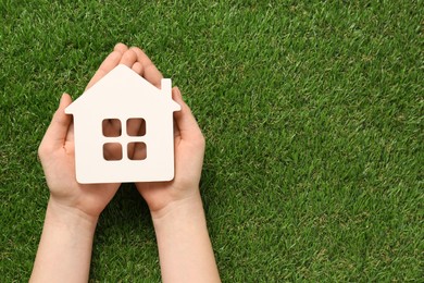 Photo of Woman holding house figure on green grass, top view. Space for text