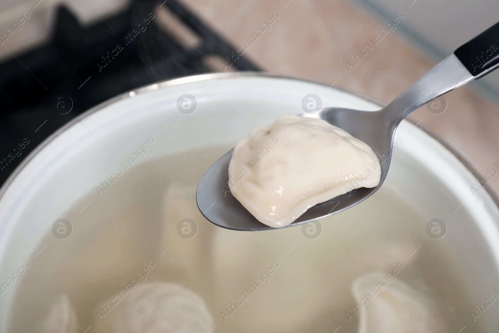 Photo of Spoon with tasty dumpling (varenyk) over pot indoors, closeup