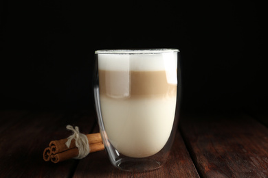 Photo of Delicious latte macchiato and cinnamon on wooden table against black background