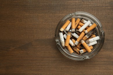 Photo of Glass ashtray with cigarette stubs on wooden table, top view. Space for text