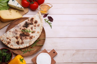 Photo of Delicious calzone and products on light wooden table, flat lay. Space for text