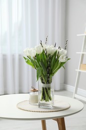 Photo of Beautiful bouquet of willow branches and tulips in vase on table indoors