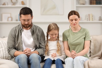 Photo of Girl and her godparents praying together on sofa at home