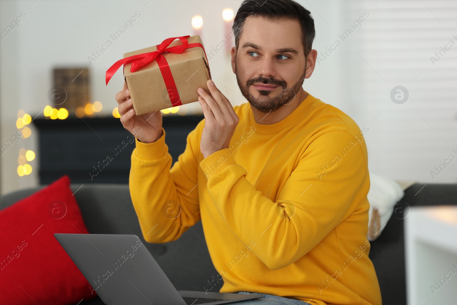 Photo of Celebrating Christmas online with exchanged by mail presents. Man with gift box during video call on laptop at home