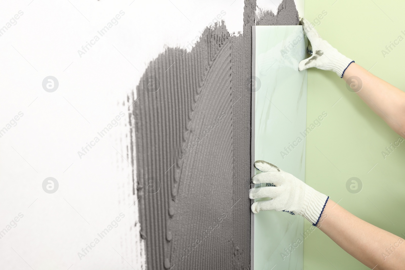 Photo of Worker installing ceramic tile on wall, closeup. Space for text
