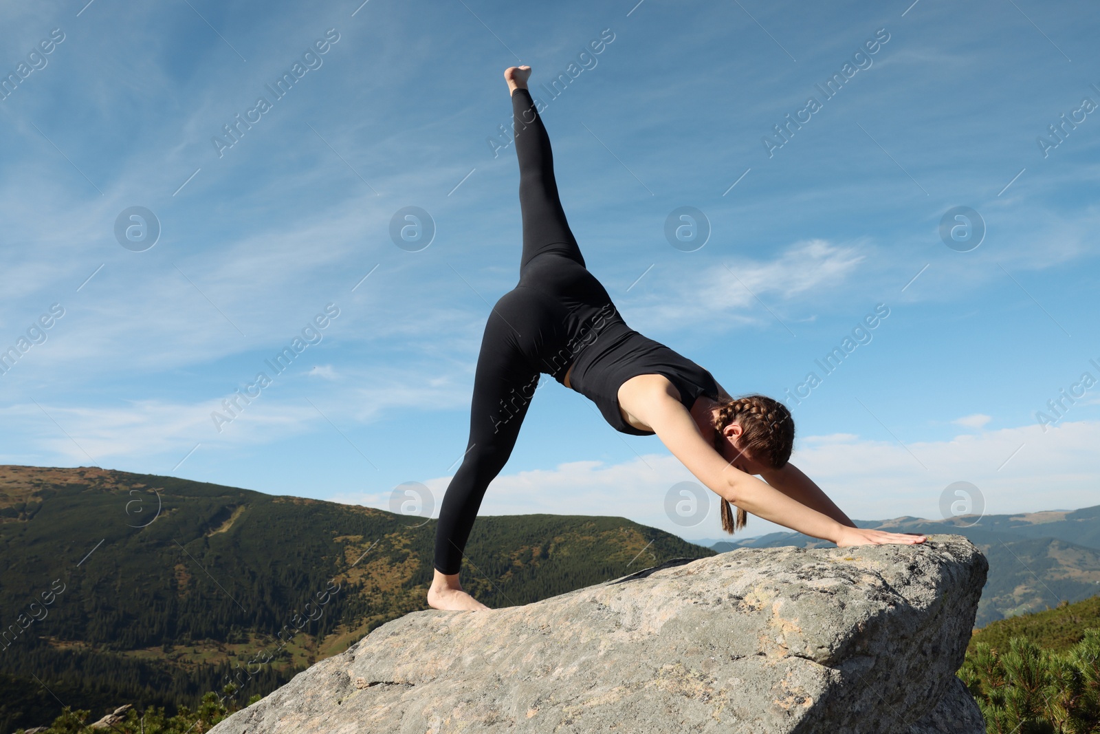 Photo of Beautiful young woman practicing yoga on rock in mountains