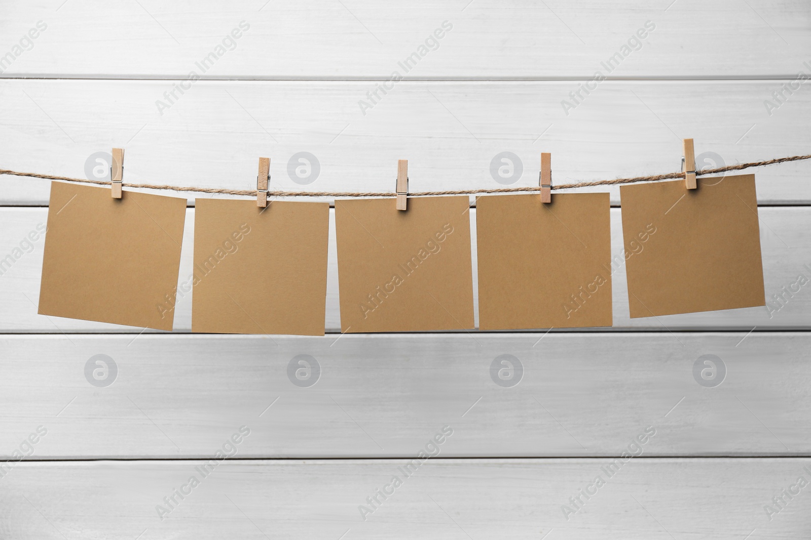 Photo of Clothespins with blank notepapers on twine against white wooden background. Space for text