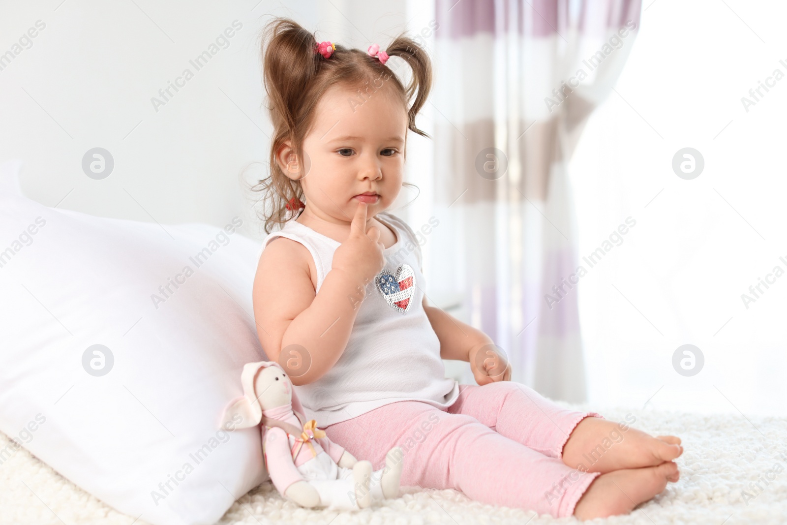 Photo of Adorable little baby girl sitting on bed in room