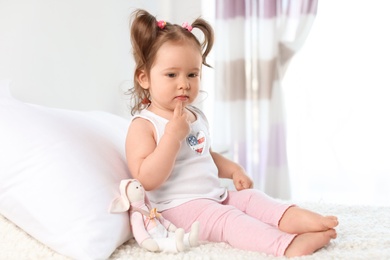 Adorable little baby girl sitting on bed in room