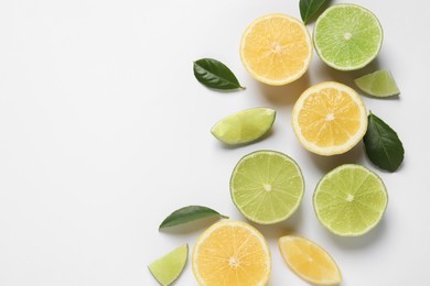 Fresh ripe lemons, limes and green leaves on white background, top view