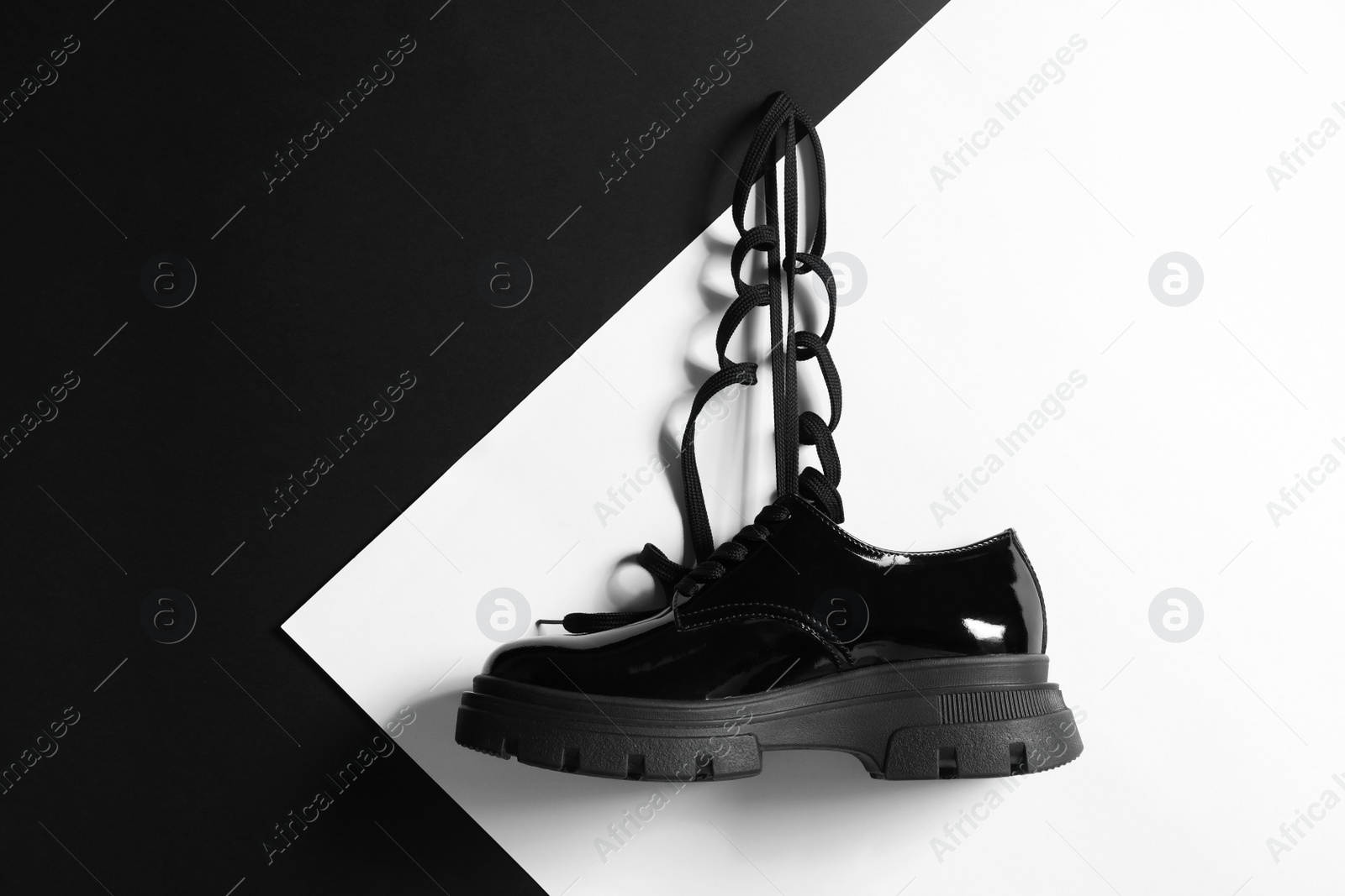 Photo of Stylish leather shoe with black lace hanging on color wall