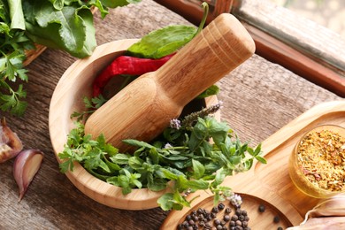 Photo of Mortar with pestle, fresh green herbs and different spices on wooden table, above view