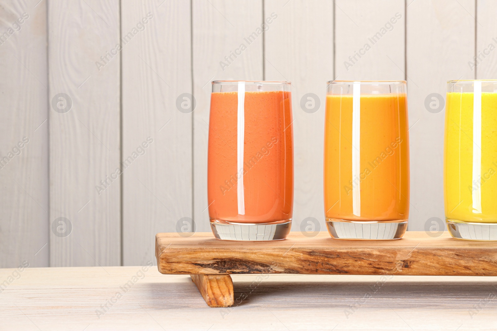 Photo of Board with many different tasty smoothies against white wooden background, space for text