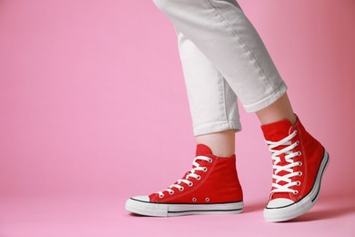 Photo of Woman wearing pair of new stylish sneakers on pink background, closeup. Space for text