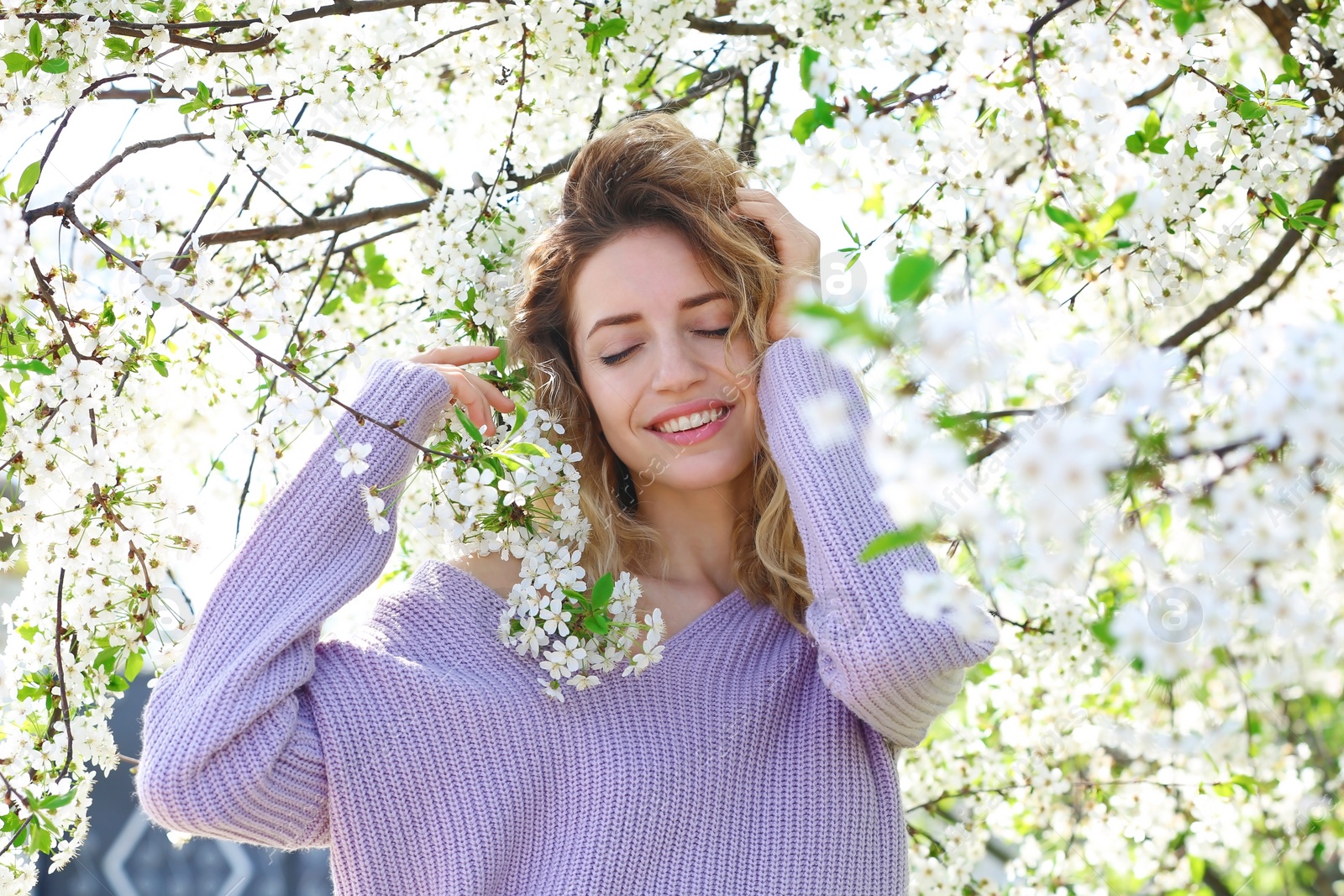 Photo of Attractive young woman posing near blossoming tree on sunny spring day