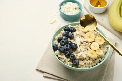 Photo of Tasty oatmeal with banana, blueberries, coconut flakes and honey served in bowl on beige table, space for text