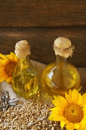 Photo of Bottles of sunflower oil, seeds and flowers on table, closeup